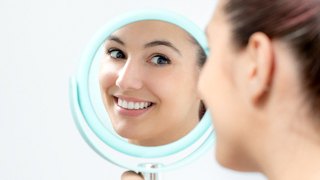 A young woman looking at her new and improved smile in a handheld mirror