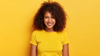 A young woman wearing a yellow t-shirt and smiling with a small gap between her upper two front teeth