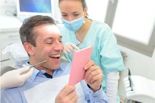 Patient with dental bridge in The Colony looking at teeth in mirror