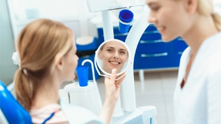 A patient looking at her smile in the mirror with her dentist next to her