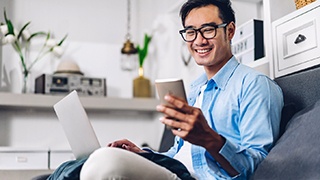 a person sitting on their couch with their laptop in their lap and phone in their hands