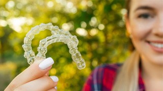 Teenage girl smiling while holding clear aligners