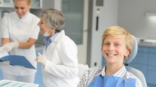 boy smiling while sitting in treatment chair next to dentist