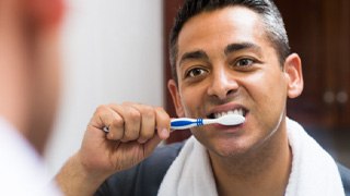 man brushing teeth in bathroom mirror