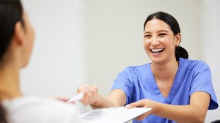 Dental assistant smiling while handing patient form 