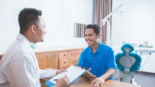 Dentist filling out forms on clipboard while talking to smiling patient