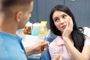 Woman in dental chair holding cheek in pain