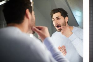 man looking at his loose tooth in the mirror 